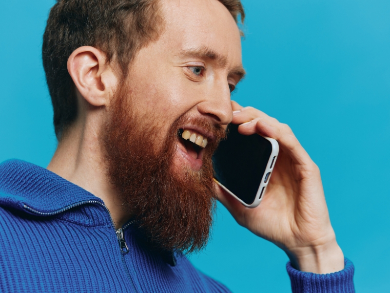 A man with a beard holding a phone to his ear and speaking